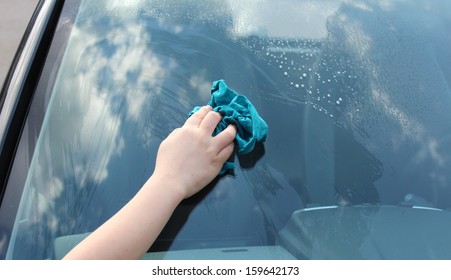 Boy cleans the window of a car