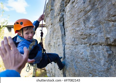 Boy Climber Gives Five. The Kid In The Helmet Climbs On The Rock. Child In Sports Outdoors.
