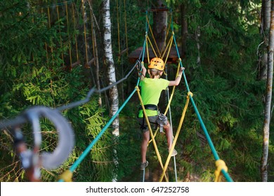 Boy Climbs In A High Wire Park Above The Ground. Ziplining. Boy On The Zip Line. Kid Passes The Rope Obstacle Course. Back View