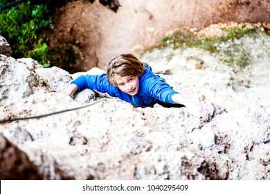 The Boy Climbs The Rock. The Child Is Engaged In Rock Climbing On A Natural Relief. The Sports Kid Actively Spends Time. Exercise In The Fresh Air.