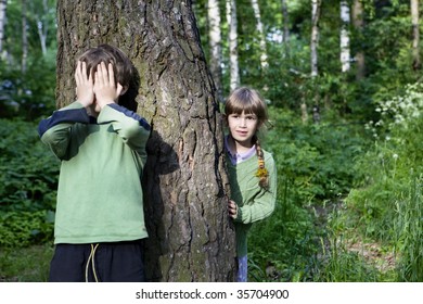 boy close his eyes by hand. Girl look out tree. Hide-and-seek