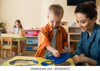 boy combining earth map puzzle near smiling teacher and girl on blurred background - Powered by Shutterstock