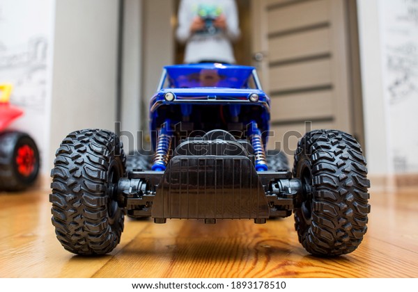 The boy is controling the blue toy\
car with a remote control. Child play with a toy\
car.