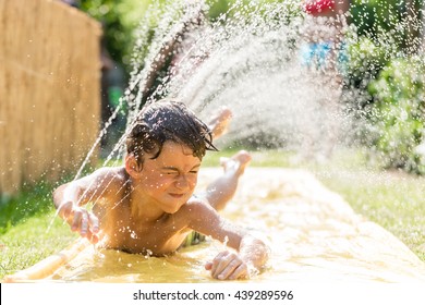 Boy cooling down with garden hose, family in the background on a hot summer day