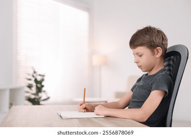 Boy with correct posture doing homework at wooden desk indoors