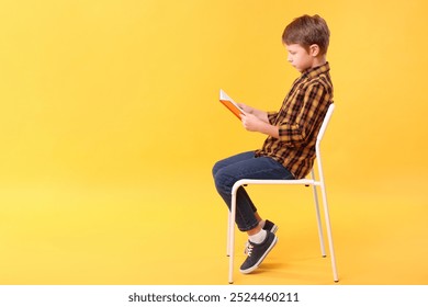Boy with correct posture reading book on chair against yellow background