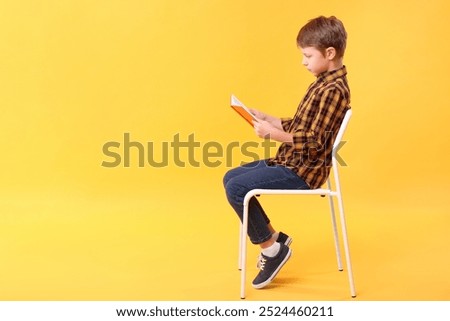 Boy with correct posture reading book on chair against yellow background