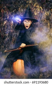 A Boy In A Costume Of Wizard With His Magic Wand Conjures Using Magic Book.  Halloween Concept. 