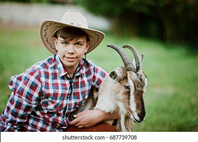 A boy in cowboy wear feeding goat with carrot in farm. teenager holding a goat in the hands on the ranch at sunset