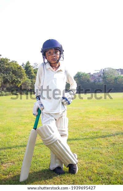Boy in cricket\
uniform holding a cricket bat\
