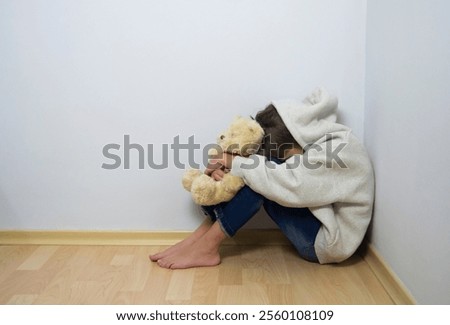 Boy crying with his head down and sitting sad scared on the floor in the corner and hugs his knees. Concept domestic violence and child abuse. 