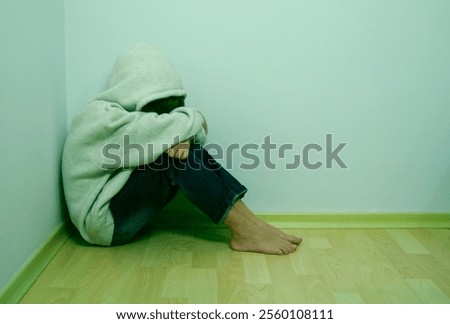 Boy crying with his head down and sitting sad scared on the floor in the corner and hugs his knees. Concept domestic violence and child abuse. 