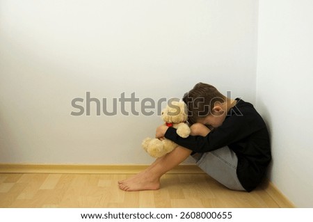 Boy crying with his head down and sitting sad scared on the floor in the corner and hugs his knees. Concept domestic violence and child abuse.