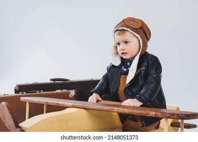 The Boy Is Crying In A Leather Jacket And A Pilot's Hat, A Wooden Plane, Brown Suitcases. Children's Wooden Toys. Baby Emotions