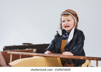 The Boy Is Crying In A Leather Jacket And A Pilot's Hat, A Wooden Plane, Brown Suitcases. Children's Wooden Toys. Baby Emotions