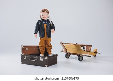 The Boy Is Crying In A Leather Jacket And A Pilot's Hat, A Wooden Plane, Brown Suitcases. Children's Wooden Toys. Baby Emotions