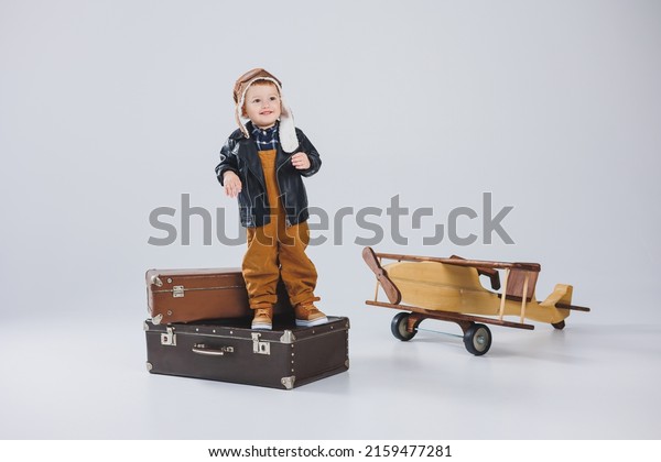 The boy is crying in a leather jacket and a\
pilot\'s hat, a wooden plane, brown suitcases. Children\'s wooden\
toys. Baby emotions