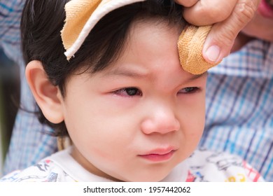 Boy Is Crying Out Of Pain. Child Bumps The Head Against Solid. Baby Is Bulging. Adult Is Wrapping Ice Cube In Cold Compress On Child. Closeup, Crying Son Face From Injury Caused By Home Accident.