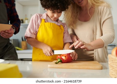 Boy Cutting Red Bell Pepper Rings Under Control Of His Parents