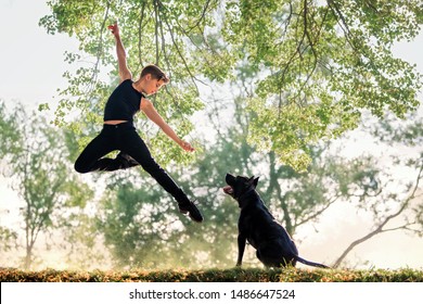 The boy dancer is jumping. The black dog is looking at the boy.
