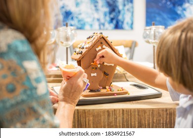 Boy decorating Halloween gingerbread house in the fall month of October using sweet candy ghost and bats in orange, black, and white plus orange icing and black frosting