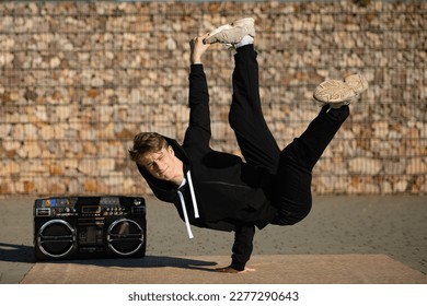 A boy in a difficult breakdancing position. A break dancer in a pose by the boombox. A boy dancing in the street.