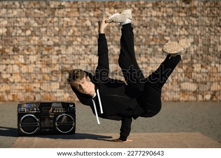 A boy in a difficult breakdancing position. A break dancer in a pose by the boombox. A boy dancing in the street.