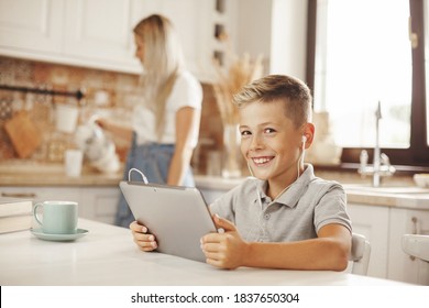 The boy does his homework in the kitchen on the tablet online, talking with the teacher. Mom cooks and helps her son. Distance learning, online education, home schooling concept - Powered by Shutterstock