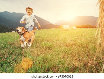 Boy and dog run together on the field with haystacks