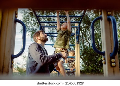 a boy doing chin-ups on monkey bars and father is helping him. Exercises on the playground on the beach. father's day concept. Image with selective focus - Powered by Shutterstock
