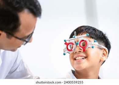 Boy doing an eye test checking examination with optometrist in the optical shop, Smiling Indian-thai boy choosing glasses in an optics store - Powered by Shutterstock