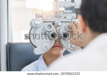 Boy doing eye test checking examination with optometrist in optical shop, Optometrist doing sight testing for child patient in clinic