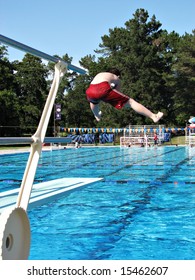 Boy Doing A Funny Jump Off The Diving Board At A Public Swimming Pool.