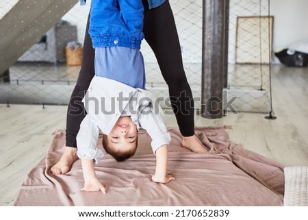 Boy doing a handstand with mother's help while playing at home in the living room
