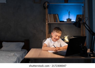 Boy Is Doing Homework Using A Laptop Computer At His Bedroom Desk At Night, Close Up