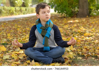 Boy doing meditation exercise sit in the yellow autumn leaves. A long scarf is tied around the boy's neck