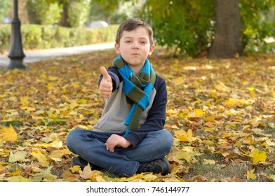 Boy doing meditation exercise sit in the yellow autumn leaves. A long scarf is tied around the boy's neck