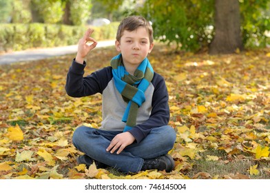 Boy doing meditation exercise sit in the yellow autumn leaves. A long scarf is tied around the boy's neck