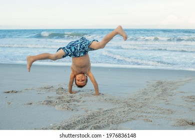 Boy doing a somersault on the sand on the beach. Exciting child having fun on the beach. Vacations by the sea. Outdoor activities with children. Summer swimming.
