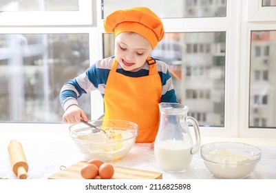 A boy with Down syndrome cooks dough from flour and milk in the kitchen, type 21 trisonomy, a genetic anomaly, a child in a chef's costume.

