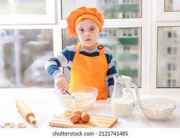 A boy with Down syndrome cooks dough from flour and milk in the kitchen, type 21 trisonomy, a genetic anomaly, a child in a chef's costume.
