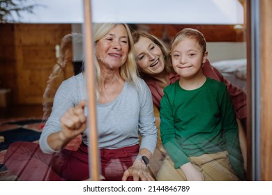Boy with Down syndrome with his mother and grandmother sitting and looking through window at home.