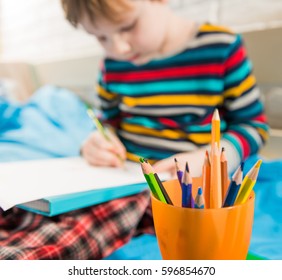 boy drawing with colorful pencils on a bed