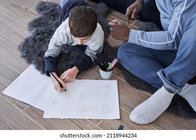 Boy drawing hand made picture and his father while sitting at the floor at cozy workplace
