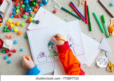 A Boy Draws A Christmas Tree. Child's Drawing Christmas. The Child Lies On The Floor And Draws In A Notebook With White Paper.