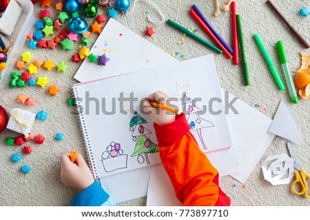 A boy draws a Christmas tree. Child's drawing Christmas. The child lies on the floor and draws in a notebook with white paper.