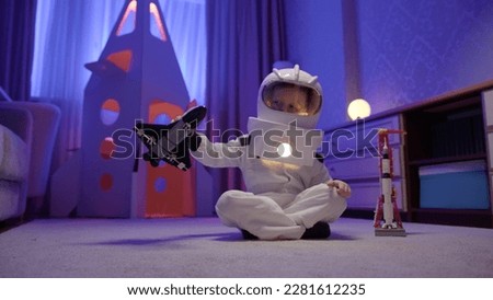 Boy dreams of becoming an astronaut and flying into space. Dream is to fly in space. Small child in an astronaut spacesuit plays at home with toy Space Shuttle orbiter.