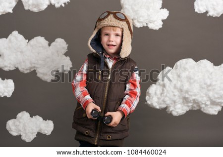 boy dressed as an airplane pilot stands between the clouds and looks through binoculars