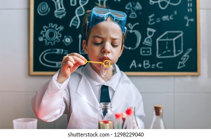 Boy dressed as chemist blowing bubbles in front of a blackboard with drawings