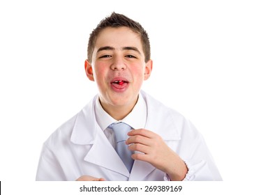 Boy dressed as a doctor in light blue tie and white coat helps to feel medicine more friendly: he is showing his tongue with a pill on it. His acne skin has not ben retouched